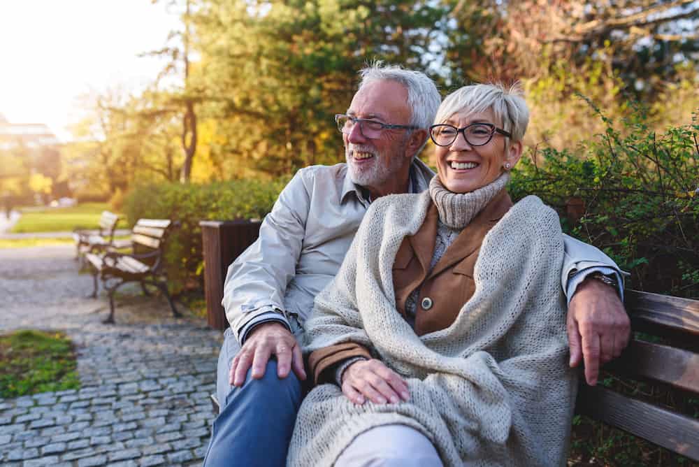 Smiling senior couple sitting on the bench in the park together enjoying retirement